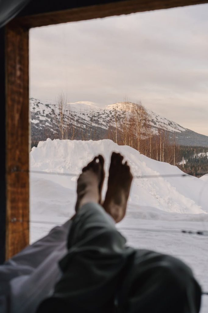 Peaceful winter morning with feet propped up, overlooking snowy mountains through a window.